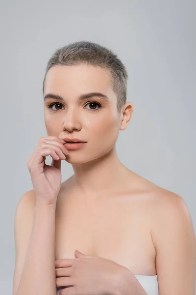 Bella donna con i capelli corti che toccano le labbra e guardando la fotocamera isolata sul grigio — Foto stock