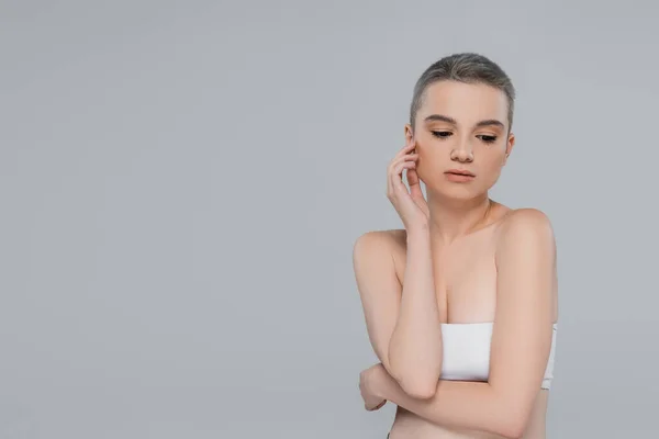 Jolie femme en haut blanc et épaules nues touchant visage isolé sur gris — Photo de stock