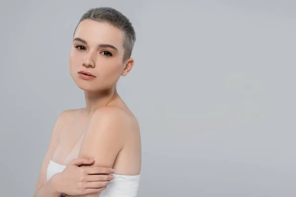 Pretty woman in white top, with naked shoulders, embracing herself isolated on grey — Stock Photo