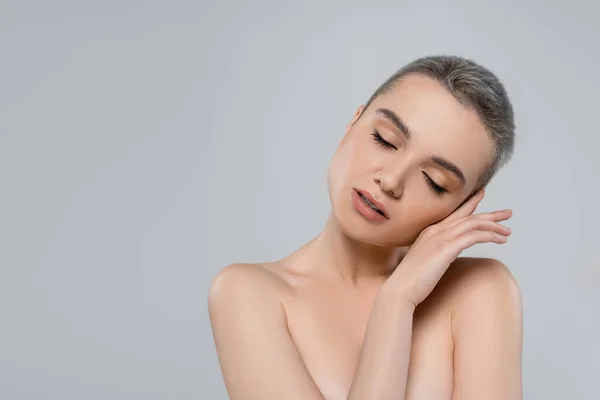 Mujer encantadora con los ojos cerrados y los hombros desnudos cogidos de la mano cerca de la cara aislada en gris - foto de stock