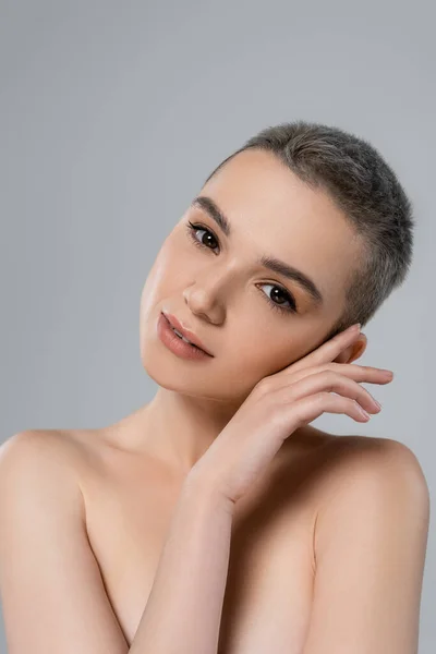 Encantadora mujer con maquillaje natural cogida de la mano cerca de la cara aislada en gris - foto de stock