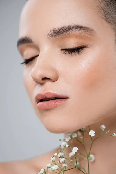 Close up view of young woman with closed eyes near white gypsophila flowers isolated on grey — Stock Photo