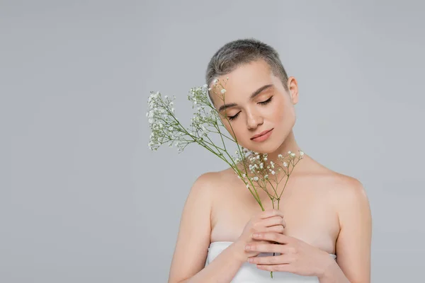 Woman with short hair and naked shoulders holding branches of gypsophila isolated on grey — Stock Photo