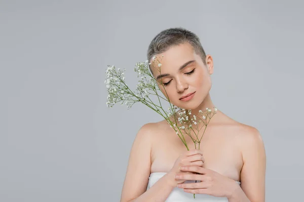 Femme aux cheveux courts et aux épaules nues tenant des branches de gypsophile isolées sur gris — Photo de stock