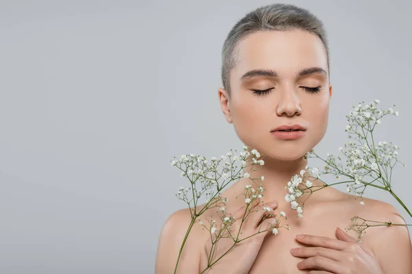 Charmante femme aux yeux fermés et aux épaules nues près des branches de gypsophile isolées sur gris — Photo de stock