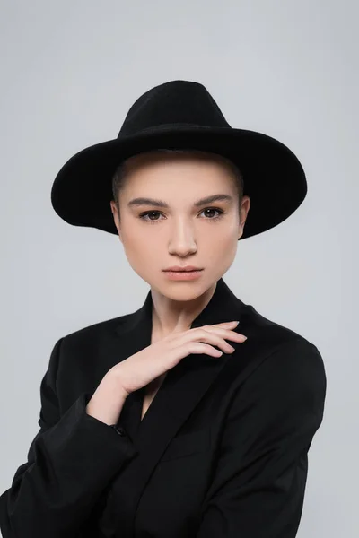 Charming woman in black blazer and brim hat looking at camera isolated on grey — Stock Photo