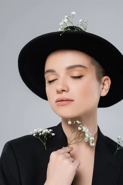 Donna elegante con gli occhi chiusi e trucco naturale in posa con fiori di gypsophila isolati su grigio — Foto stock