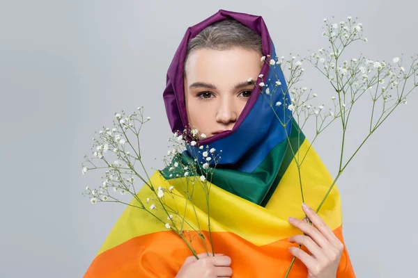 Woman with lgbt flag on head holding gypsophila flowers isolated on grey — Stock Photo