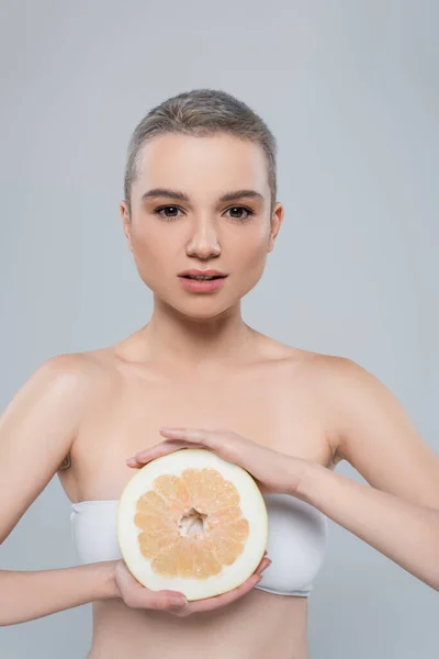 Charming woman with perfect skin and bare shoulders holding ripe grapefruit isolated on grey — Stock Photo