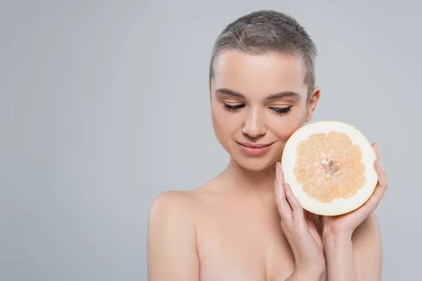 Smiling woman with naked shoulders holding half of ripe grapefruit isolated on grey — Stock Photo