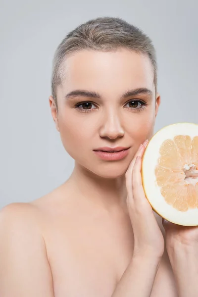 Ritratto di giovane donna con metà pompelmo succoso guardando la fotocamera isolata su grigio — Foto stock