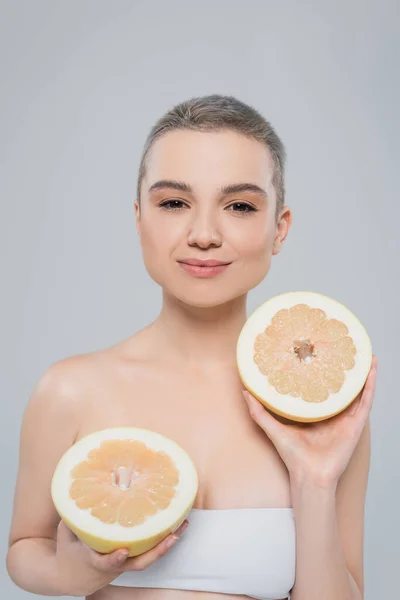 Задоволена жінка з ідеальною шкірою, що тримає половинки соковитих грейпфрутів ізольовані на сірому — стокове фото