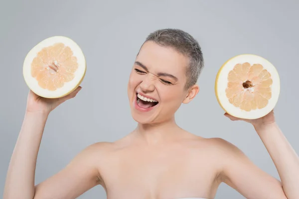 Задоволена жінка з ідеальною шкірою, що тримає половинки соковитих грейпфрутів ізольовані на сірому — стокове фото