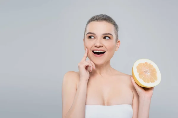 Erstaunte Frau mit Grapefruit blickt in Kamera isoliert auf grau — Stockfoto