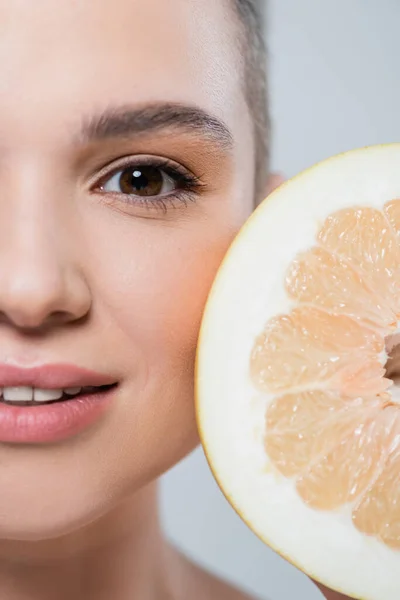 Крупним планом вид грейпфрута половина біля обрізаного жіночого обличчя ізольовано на сірому — стокове фото