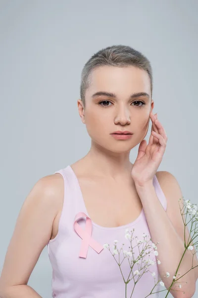 Mujer bonita con la cinta de la conciencia del cáncer de pecho en la tapa del tanque y flores diminutas blancas aisladas en gris - foto de stock