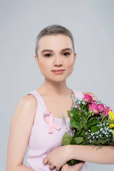 Woman with breast awareness ribbon on tank top holding colorful bouquet isolated on grey — Stock Photo