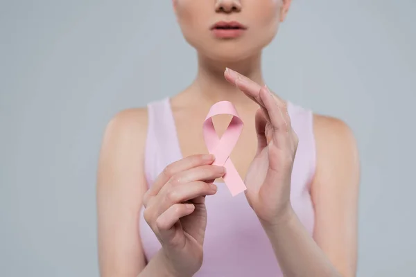 Vista cortada de mulher desfocada segurando fita consciência rosa isolado em cinza — Fotografia de Stock