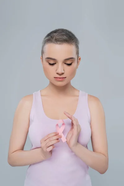 Jeune femme en débardeur tenant un ruban de sensibilisation au cancer du sein isolé sur gris — Photo de stock