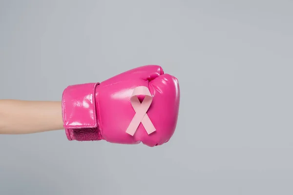 Vista parcial de la mano femenina con cinta de sensibilización sobre el cáncer de mama en guante de boxeo rosa aislado en gris - foto de stock