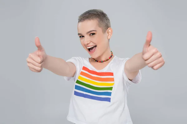 Joyful woman in rainbow colors t-shirt showing thumbs up isolated on grey — Stock Photo