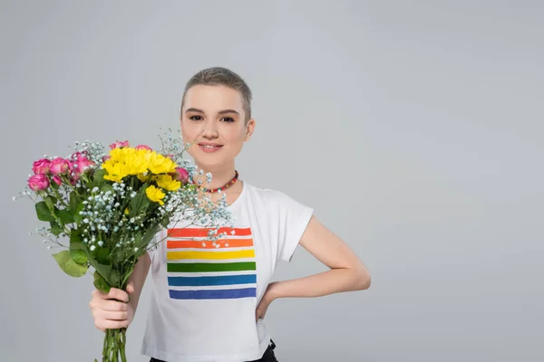 Щаслива жінка в футболці кольорів lgbt, що тримає квіти ізольовані на сірому — стокове фото