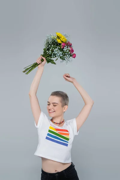 Joyeuse femme en lgbt couleurs t-shirt tenant bouquet dans les mains levées isolé sur gris — Photo de stock