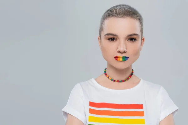 Vorderseite der hübschen Frau in lgbt Farben T-Shirt und Halskette Blick auf Kamera isoliert auf grau — Stockfoto