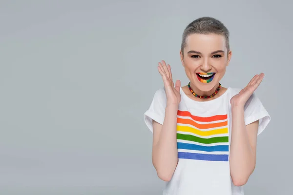 Mujer alegre en color arco iris camiseta mirando a la cámara aislada en gris - foto de stock