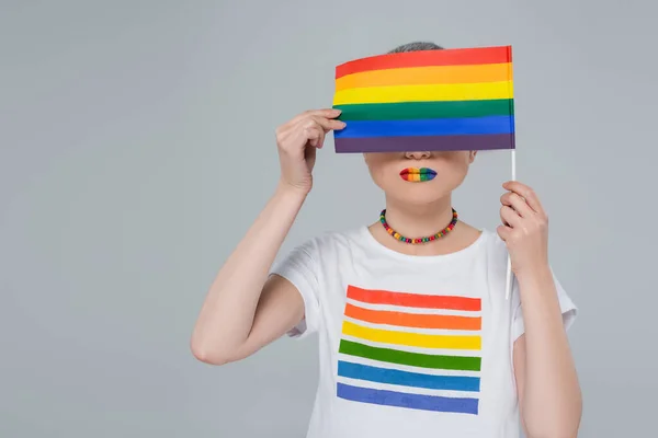Junge Frau in Regenbogenfarben T-Shirt verdeckt Gesicht mit lgbt Flagge isoliert auf grau — Stockfoto