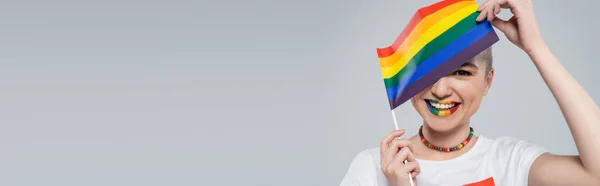 Happy woman obscuring face with small lgbt flag isolated on grey, banner — Stock Photo