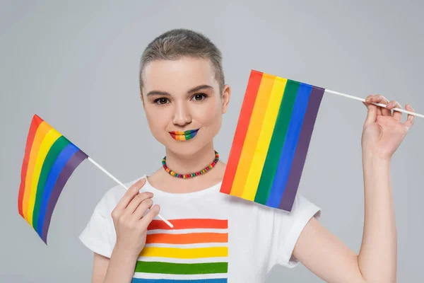 Hübsche Frau mit Regenbogenfarben Lippen halten kleine lgbt Flaggen isoliert auf grau — Stockfoto