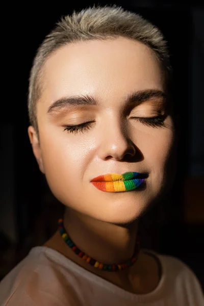 Nahaufnahme Porträt einer Frau mit regenbogenfarbenen Lippen und geschlossenen Augen isoliert auf schwarz — Stockfoto