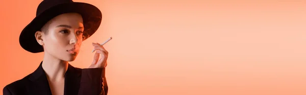 Encantadora mujer en sombrero de ala negra fumando y mirando hacia otro lado sobre el fondo de coral, pancarta - foto de stock