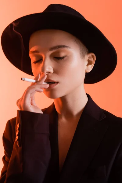 Sensual and stylish woman with closed eyes smoking on coral background — Stock Photo