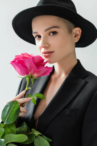 Elegant woman in black brim hat holding pink rose and looking at camera isolated on grey — Stock Photo