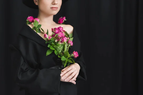 Vista recortada de mujer joven en chaqueta negra posando con rosas rosadas sobre fondo oscuro - foto de stock