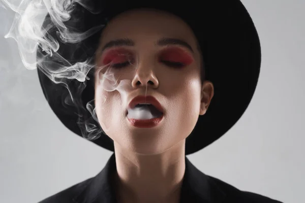 Vista frontal da mulher elegante com olhos fechados exalando fumaça isolada no cinza — Fotografia de Stock