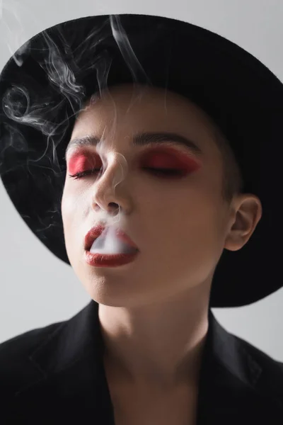 Woman with closed eyes and carmine red makeup exhaling smoke isolated on grey — Stock Photo