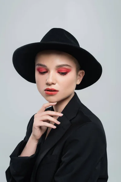 Hübsche Frau mit schwarzem Hut und Blazer, die ihr Kinn isoliert auf grau berührt — Stockfoto