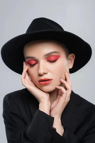 Frau mit geschlossenen Augen und karminrotem Make-up berührt Gesicht isoliert auf grau — Stockfoto