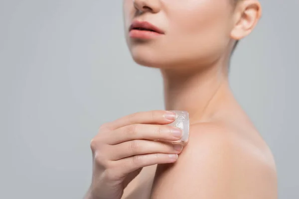 Partial view of woman with clean skin applying ice cube to bare shoulder isolated on grey — Stock Photo