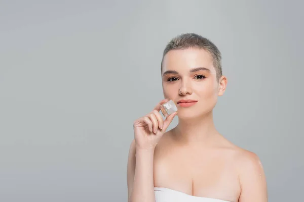 Woman with short hair and naked shoulders holding ice cube isolated on grey — Stock Photo