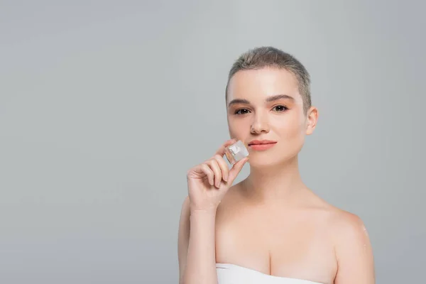 Femme aux cheveux courts et aux épaules nues tenant un glaçon isolé sur gris — Photo de stock