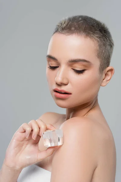 Pretty woman with natural makeup applying ice cube to bare shoulder isolated on grey — Stock Photo