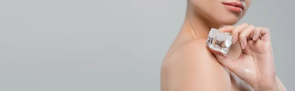 Partial view of woman applying ice cube to naked shoulder isolated on grey, banner — Stock Photo