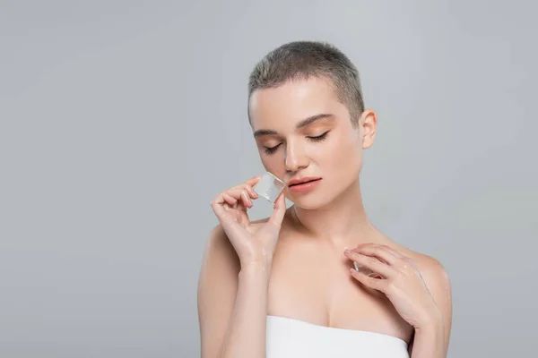Sensual woman with closed eyes and naked shoulders posing with ice cubes isolated on grey — Stock Photo