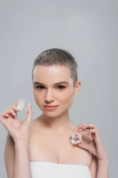 Frau mit sauberer Haut und natürlichem Make-up hält Eiswürfel isoliert auf grau — Stockfoto