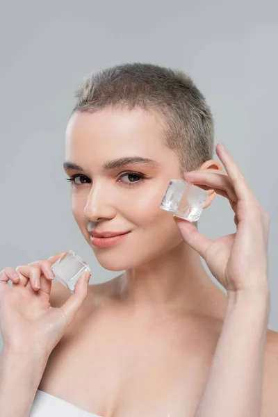 Sonriente mujer mostrando cubitos de hielo mientras mira la cámara aislada en gris - foto de stock