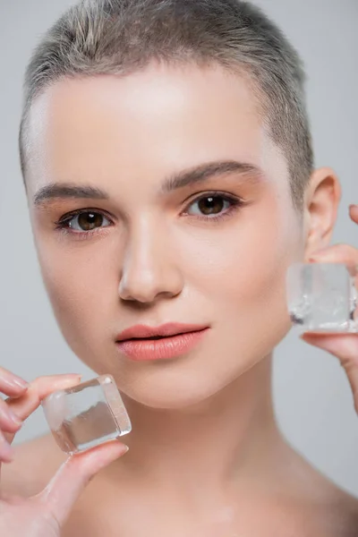 Porträt einer jungen Frau mit natürlichem Make-up in der Nähe von Eiswürfeln isoliert auf grau — Stockfoto